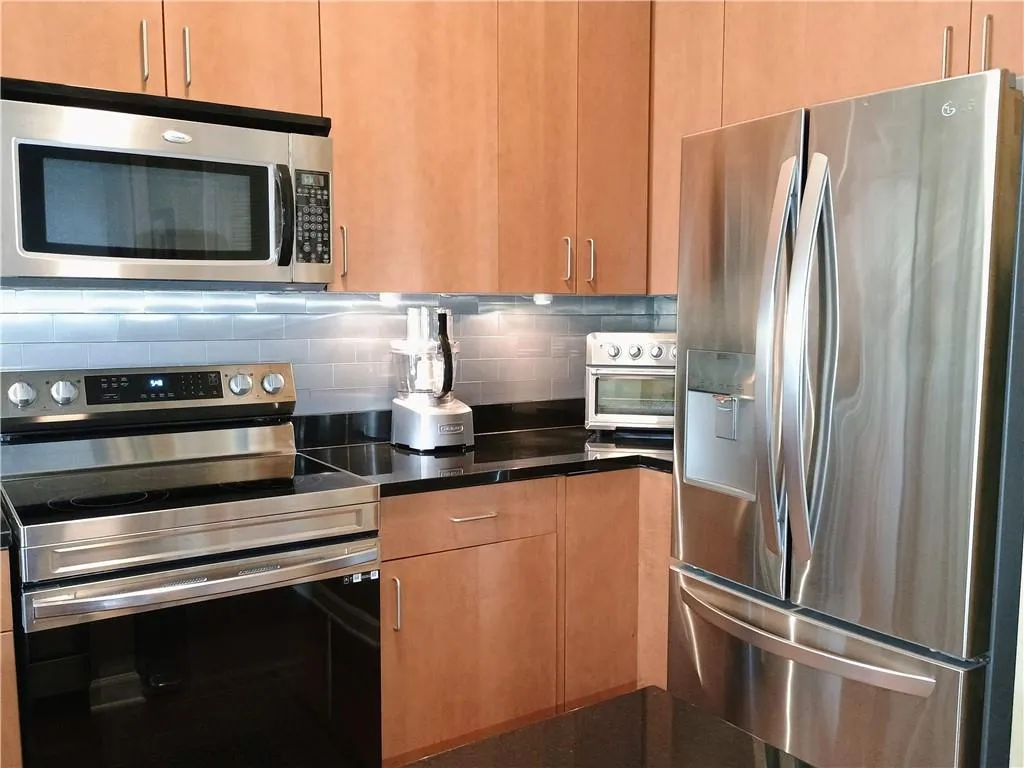Kitchen featuring  dark countertops, stainless steel appliances, and tasteful backsplash