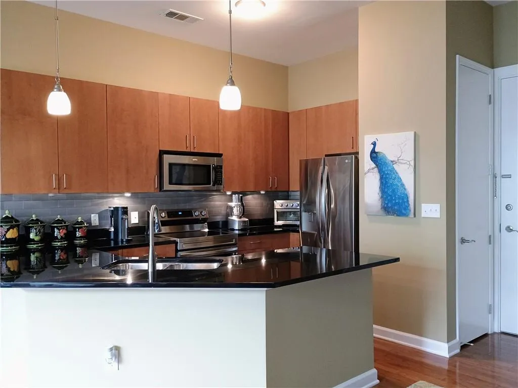 Kitchen featuring stainless steel appliances, dark countertops, a sink, visible vents, and a peninsula