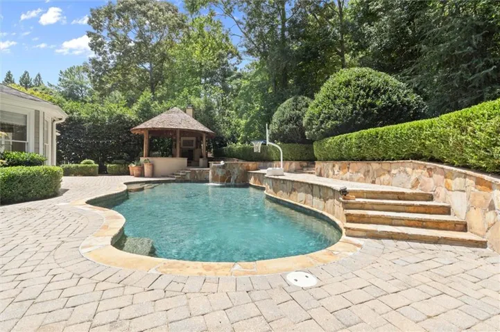 Curved swimming pool with stone coping, surrounded by a paver patio