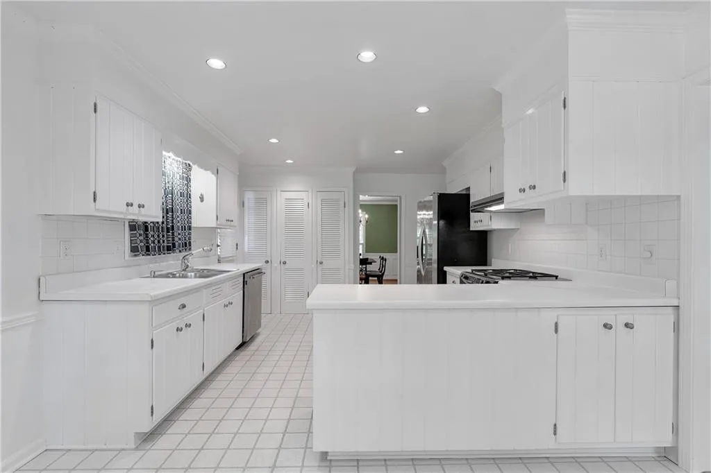Kitchen featuring kitchen peninsula, light tile flooring, white cabinetry, and appliances with stainless steel finishes