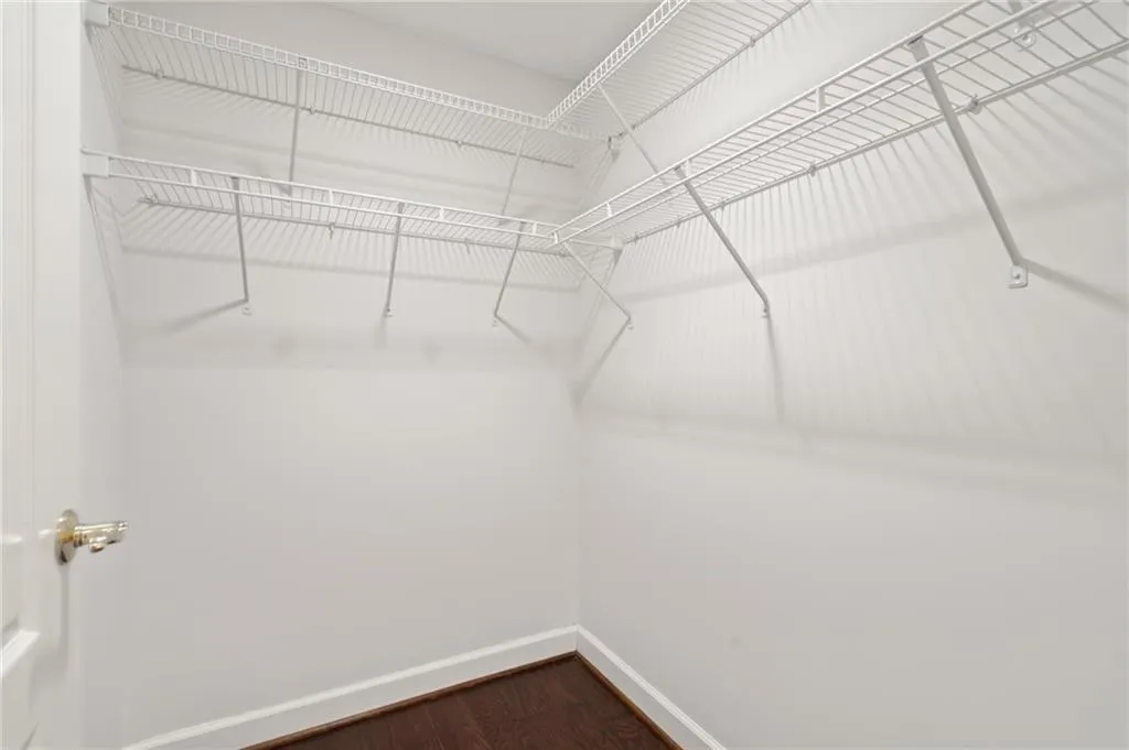 Walk-in closet with white wire shelving, dark wood-finish flooring, white baseboards, and a white interior door with a brass-finish doorknob