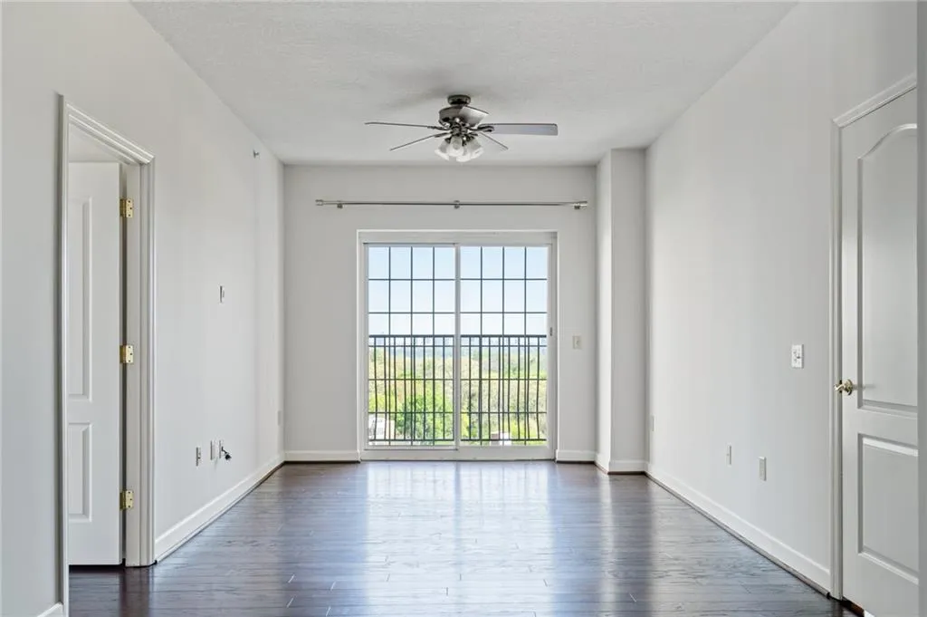 Spacious room with dark wood-finish flooring, white walls, and a sliding glass door opening to a private balcony with black metal railings
