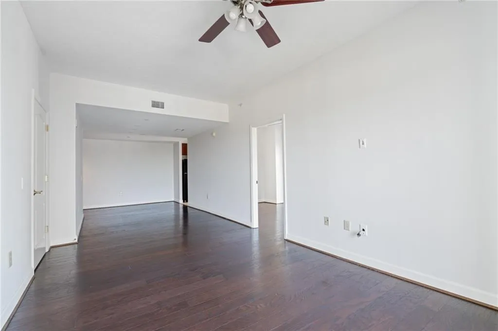 Expansive room featuring dark wood-finish flooring, white walls, and a ceiling fan with integrated lighting