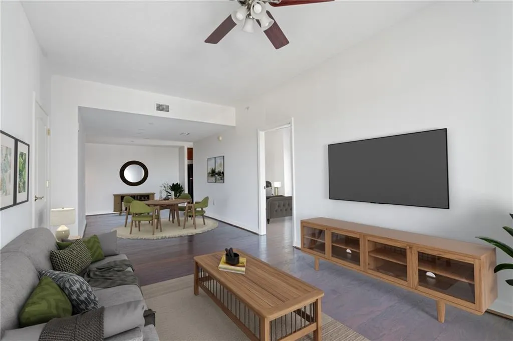 Open-concept living area featuring wood-finish flooring, a ceiling fan with integrated lighting, and a wide entryway to an additional room