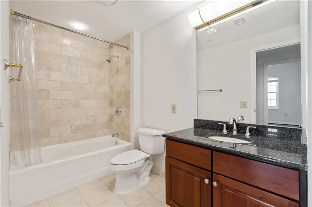 Full bathroom featuring a tub/shower combination with light-toned tile surround, a dark stone vanity top, a rectangular undermount sink, and a rich wood-finish vanity cabinet