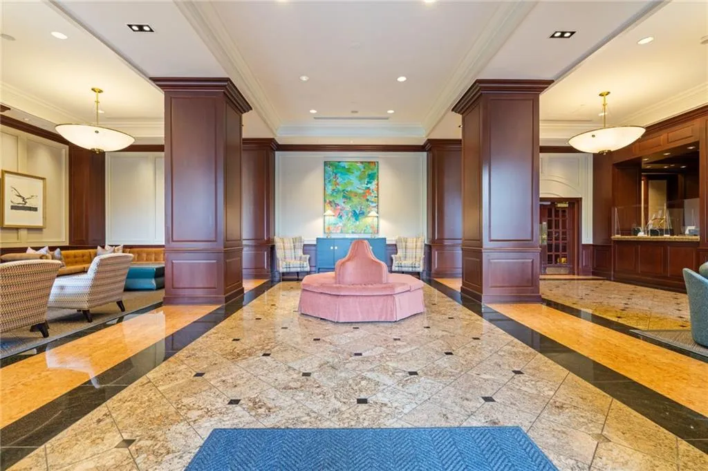 Spacious foyer featuring polished stone tile flooring with dark accent borders, dark wood paneling on columns and walls, recessed lighting, and elegant pendant light fixtures