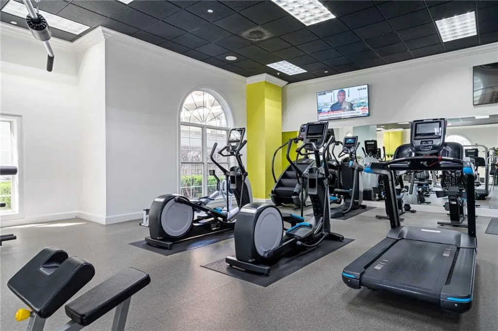 Fitness center featuring multiple exercise machines, a wall-mounted television, arched windows, and a black grid ceiling