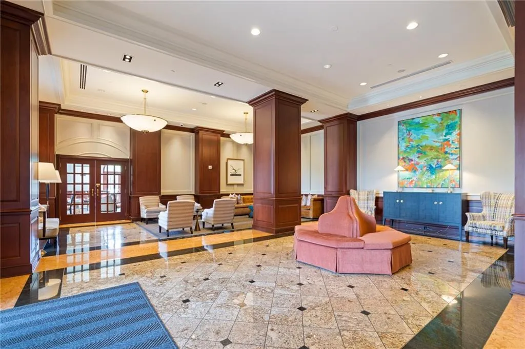Spacious lobby featuring polished stone flooring, rich wood paneling, recessed lighting, double glass-paned entry doors, and elegant pendant light fixtures