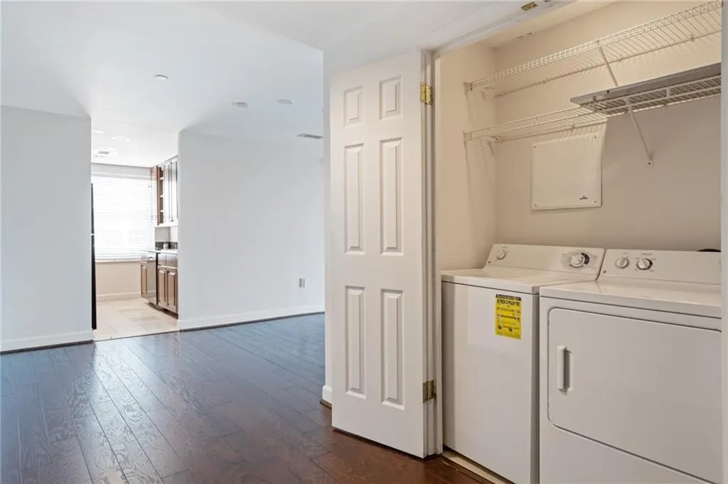 Dedicated laundry closet with wire shelving and full-size appliances, positioned alongside wood-finish flooring