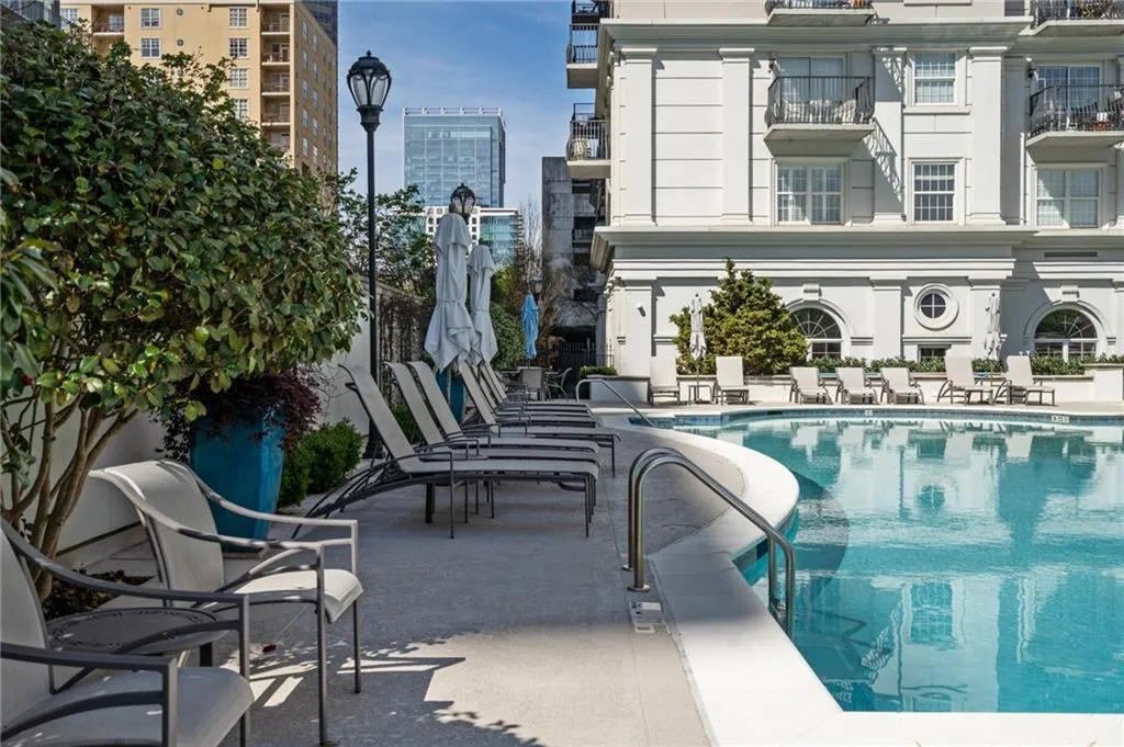 Curved swimming pool with an integrated entry handrail, surrounded by lounge chairs and umbrella-shaded seating