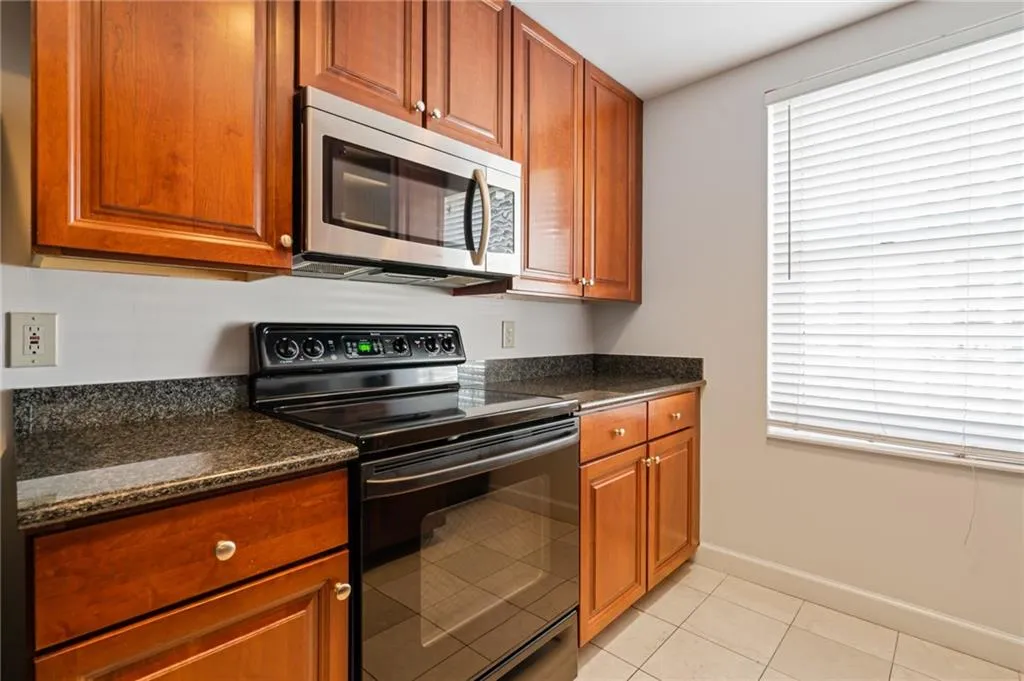 Kitchen featuring wood-finish cabinetry, granite-style countertops, stainless steel microwave, black electric range, and tile flooring