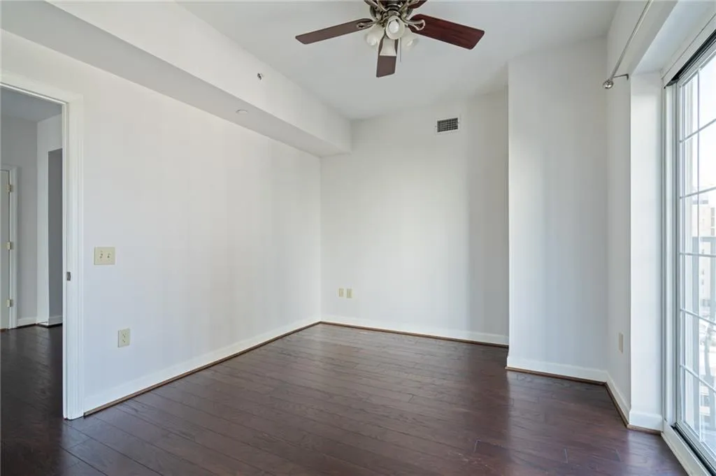 Room featuring dark wood-finish flooring, white walls, and a ceiling fan with integrated lighting
