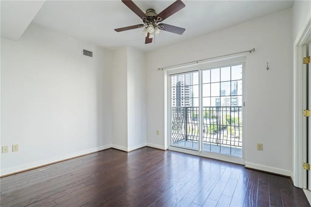 Room featuring wood-finish flooring, a ceiling fan, and a sliding glass door opening to a balcony with decorative metal railings