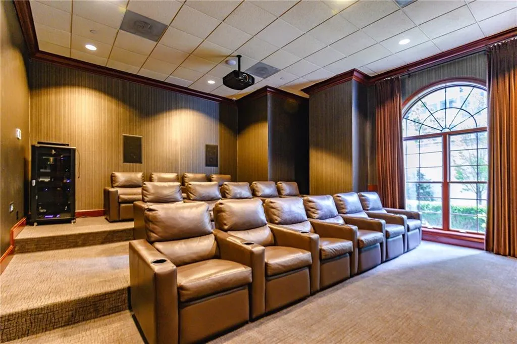 Tiered seating featuring brown leather recliners, wall-mounted speakers, recessed lighting, a ceiling-mounted projector, and an arched window with drapes