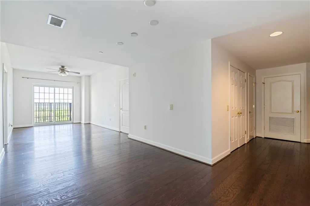 Spacious open-concept living area featuring dark wood-finish flooring, white walls, and a ceiling fan with light