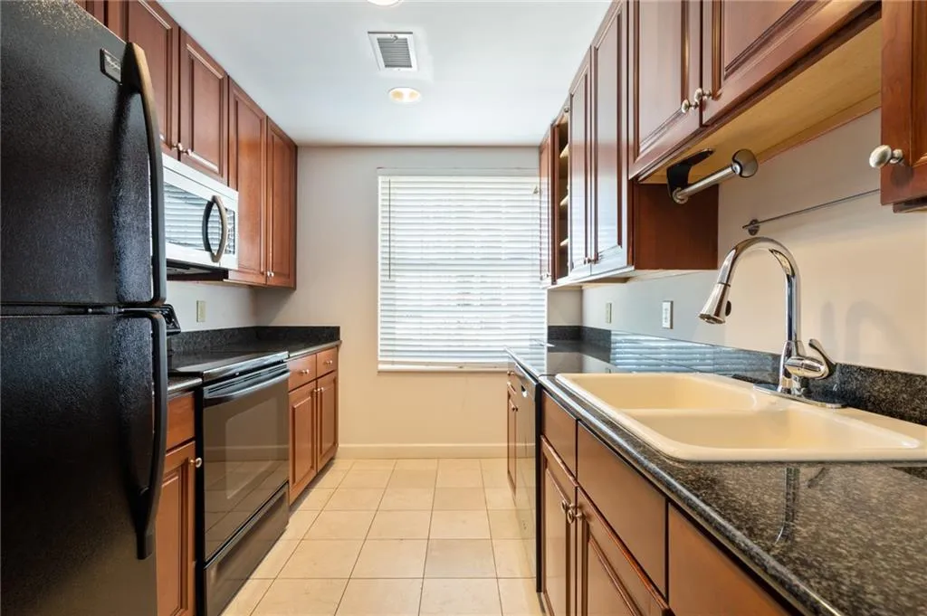 Kitchen featuring wood cabinetry, black countertops, and a dual-basin sink with a chrome faucet