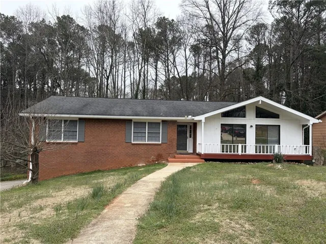 Brick ranch home featuring a covered front porch with white railings, multiple windows with dark frames, and a concrete walkway leading to the entry