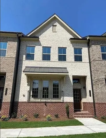 Two-story brick facade, gabled roofline, second-level balcony, covered front entry, and mature landscaping