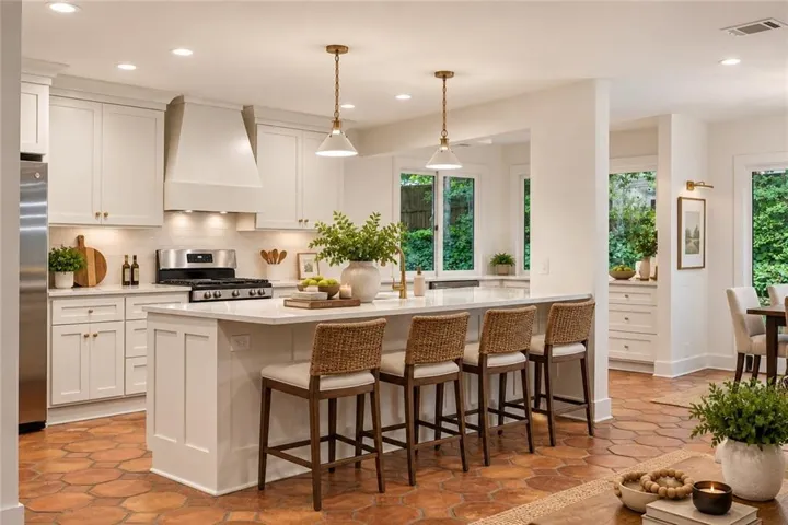 Kitchen featuring white cabinetry, a large center island with seating, a stainless steel gas range, and hexagonal terracotta-style floor tiles