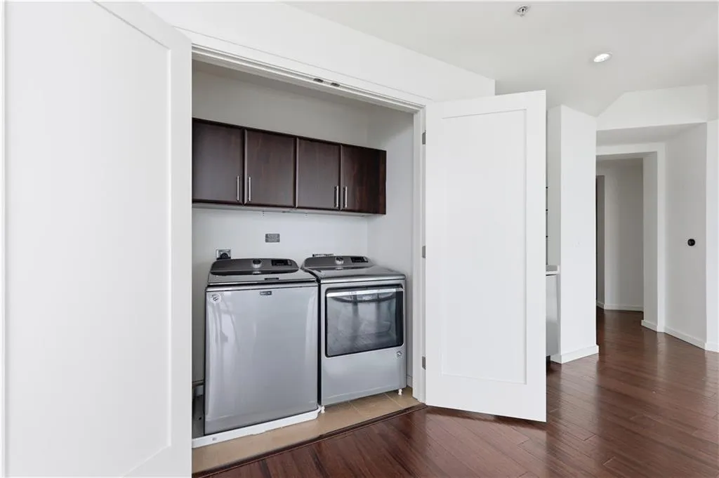 Laundry closet with dark wood-finish cabinetry, white flat-panel doors, and wood-finish flooring