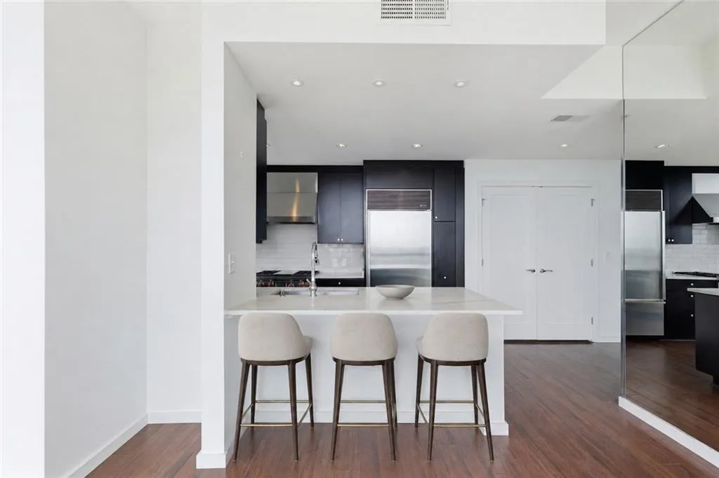VIRTUALLY STAGED-Kitchen featuring a center island with light-toned countertop, dark wood-finish flooring, stainless steel appliances, dark cabinetry, and recessed lighting