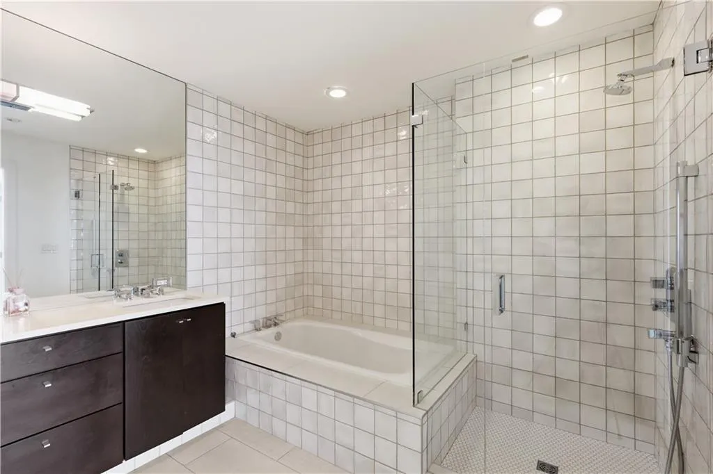 Bathroom featuring a built-in bathtub, glass-enclosed shower, dark wood-finish vanity with countertop, and an expansive wall mirror