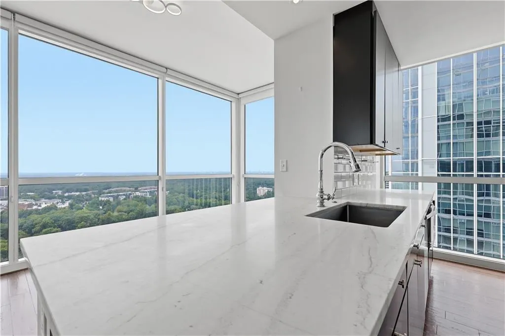 Expansive floor-to-ceiling windows, large island with integrated sink, stainless steel faucet, and wood-finish flooring