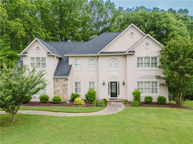 View of front of house featuring a shingled roof, a front lawn, and stone siding