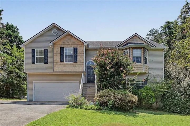 Split-level residence featuring a two-car garage, bay window, arched entry door, and mixed siding exterior