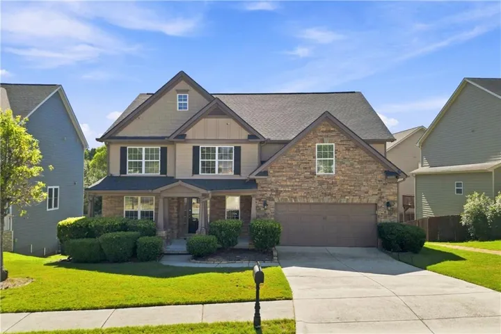 Stone and siding facade with a covered porch entry, presenting a two-car garage, multiple windows with dark shutters, and a well-maintained front lawn