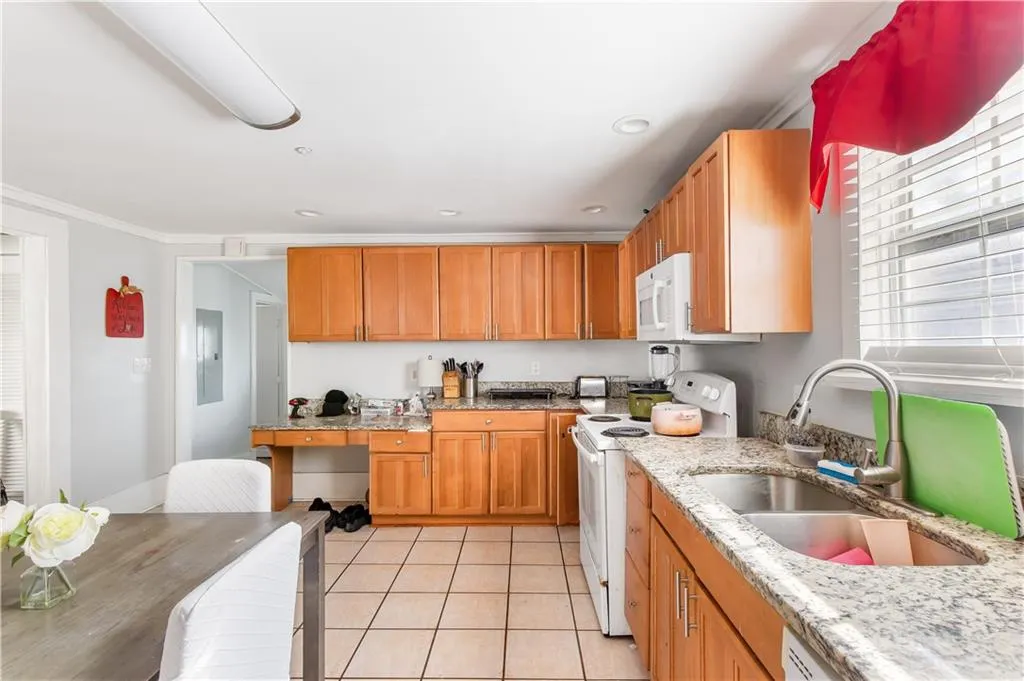 Kitchen featuring sink, light tile flooring, white appliances, and light stone countertops