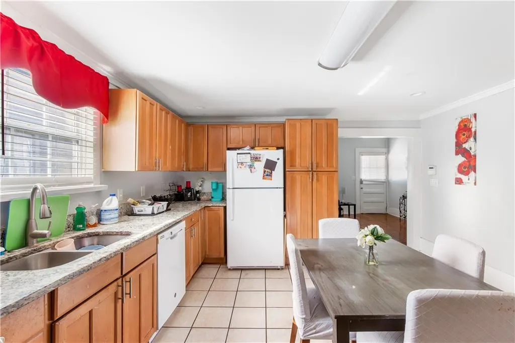 Kitchen featuring white appliances, ornamental molding, light stone counters, light tile floors, and sink
