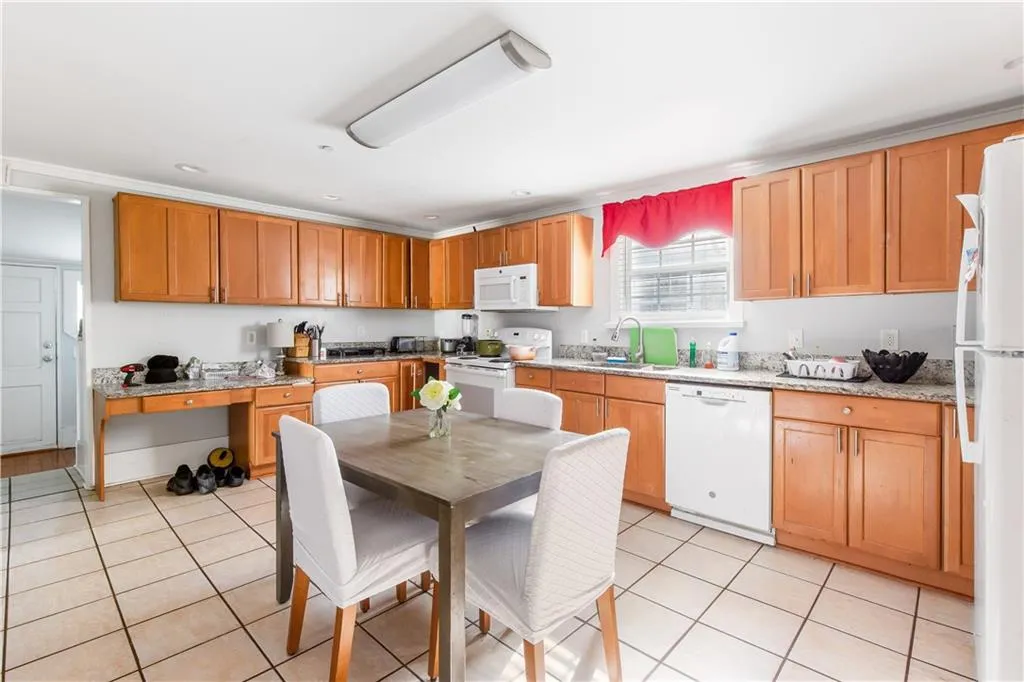 Kitchen with sink, light tile floors, white appliances, and light stone counters