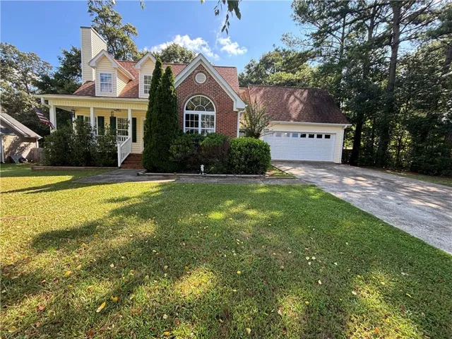 Traditional-style home featuring a brick facade accent, dormer windows, covered front porch with white railing, and a two-car garage
