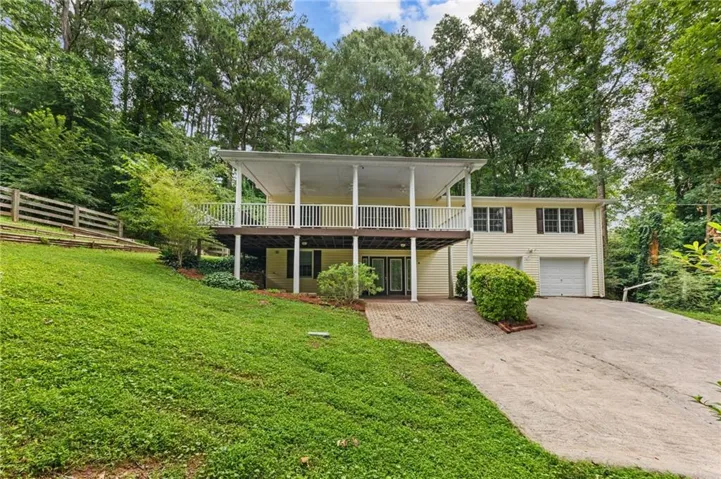 Split-level residence featuring a light-colored exterior, an upper-level covered porch with white railings, and a lower-level brick paver patio