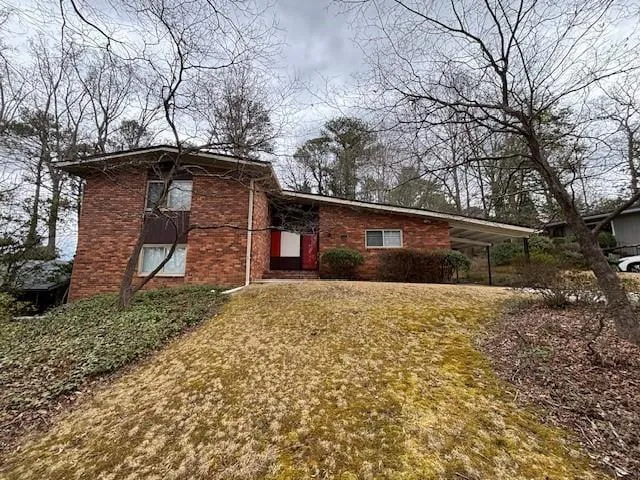 Brick exterior with a partial carport, a multi-pane window, and mature trees