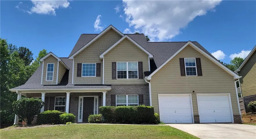 Two-story residence featuring a covered front porch, brick and siding exterior, two-car garage, and established landscaping