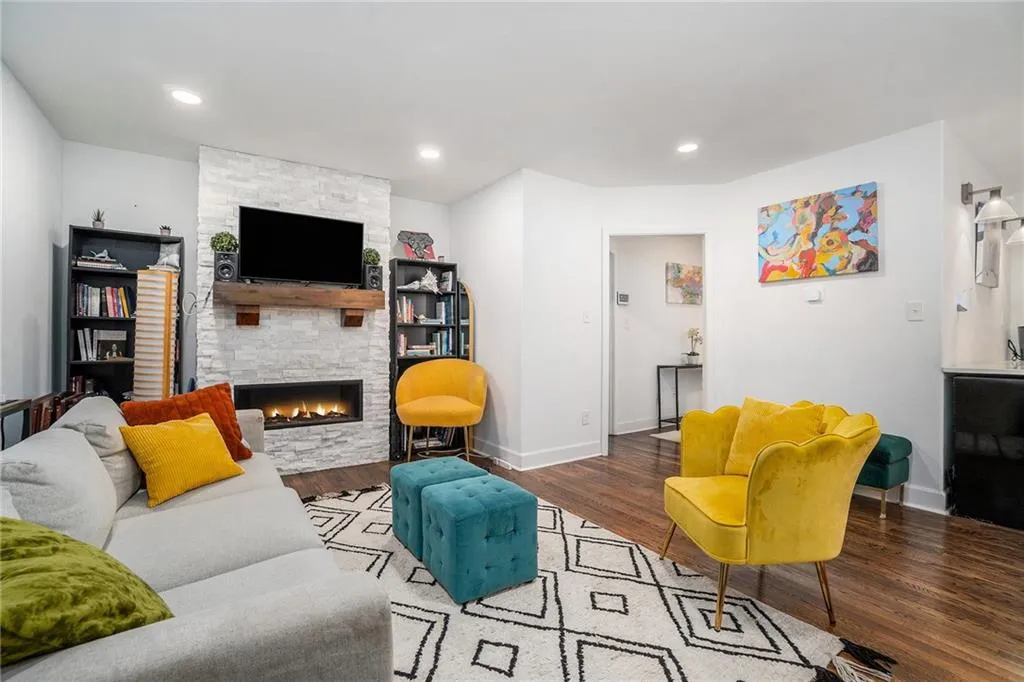 Living room with wood finished floors, a stone fireplace, and recessed lighting