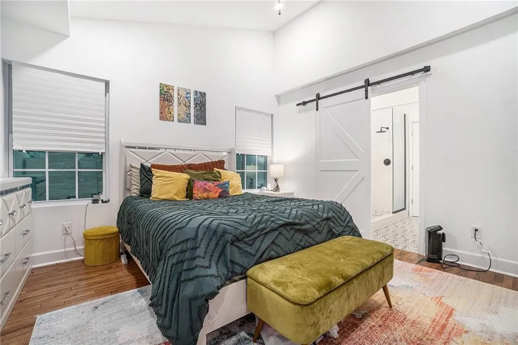 Bedroom with wood finished floors, a barn door, connected bathroom, and high vaulted ceiling