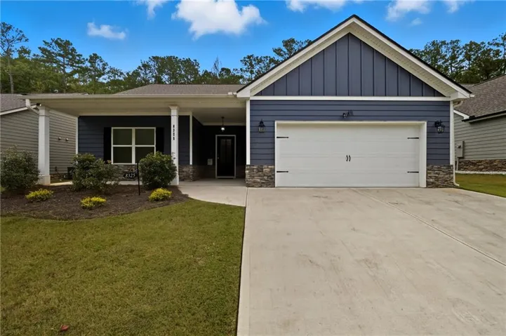 Ranch-style home featuring stone siding, board and batten siding, covered porch, driveway, and a front lawn