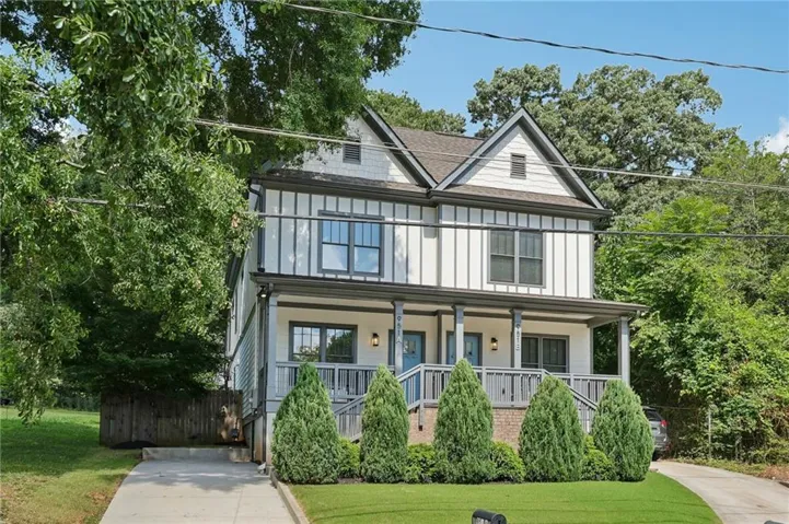 Modern farmhouse-style duplex featuring a gabled roofline, board and batten siding, a covered porch with a railing, a paved driveway, and manicured landscaping with mature trees