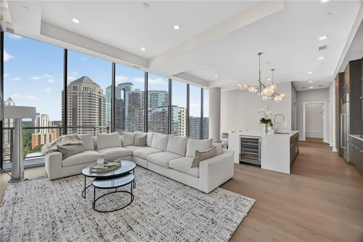 Expansive floor-to-ceiling windows, light wood-finish flooring, a contemporary kitchen island with a built-in beverage refrigerator, a modern chandelier, and recessed lighting