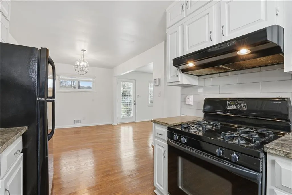 Kitchen featuring black appliances, white cabinets, light wood finished floors, backsplash, and suspended lighting