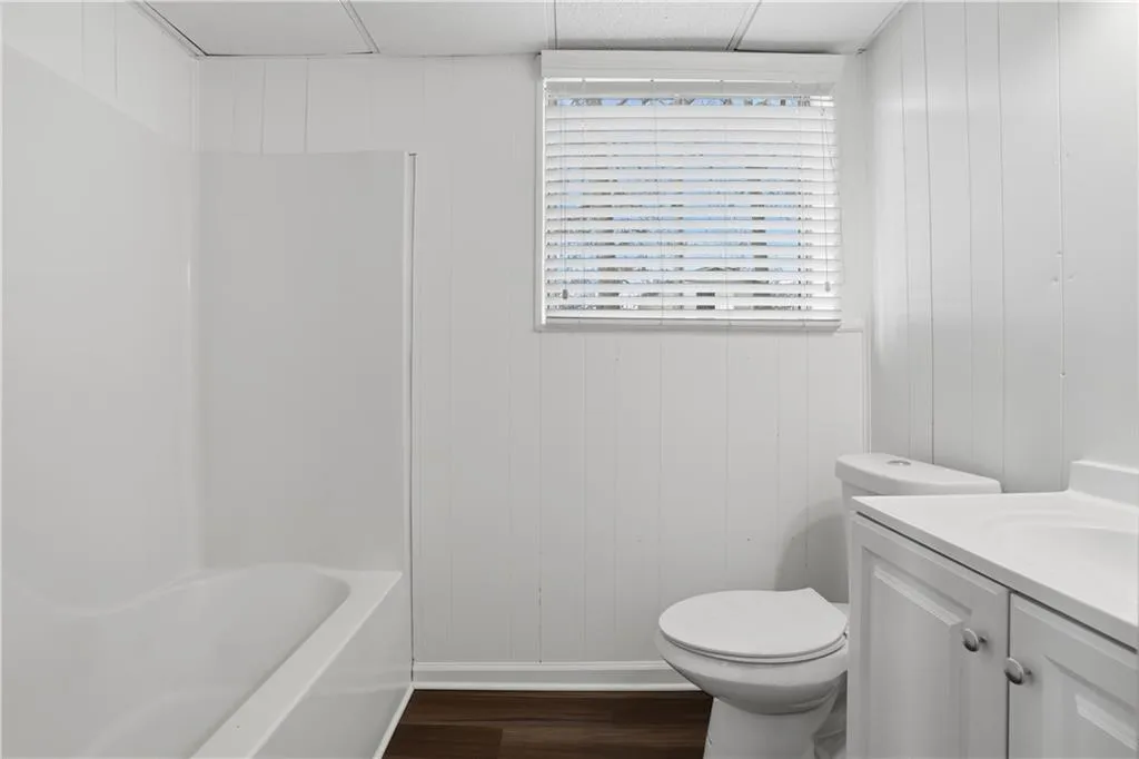 Bathroom with dark laminate floors, vanity, wood walls, and shower / bathtub combination