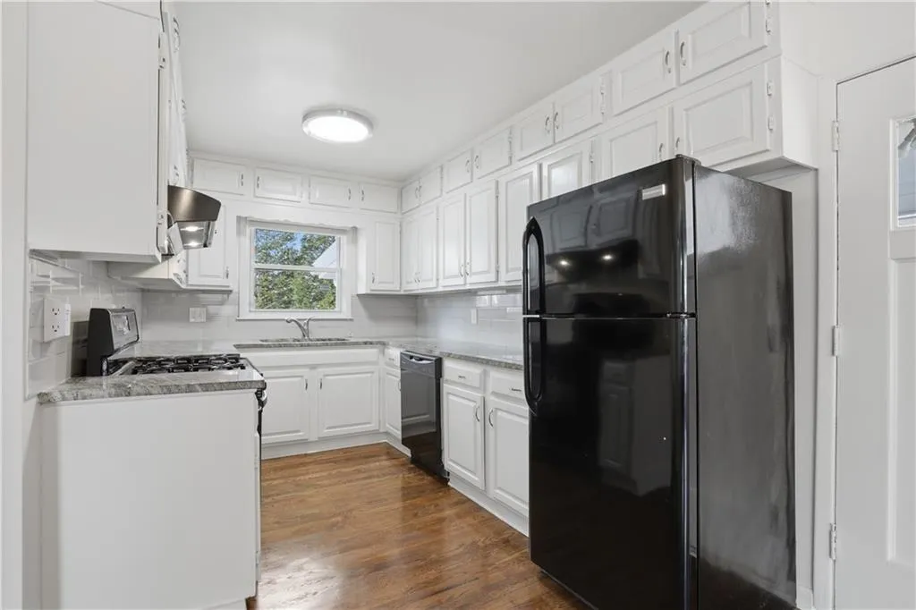 Kitchen featuring black appliances, white cabinetry, dark wood-type flooring, backsplash, and ventilation hood