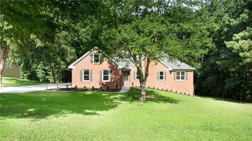 Brick residence with a gravel driveway, mature trees, and a sloped, manicured lawn