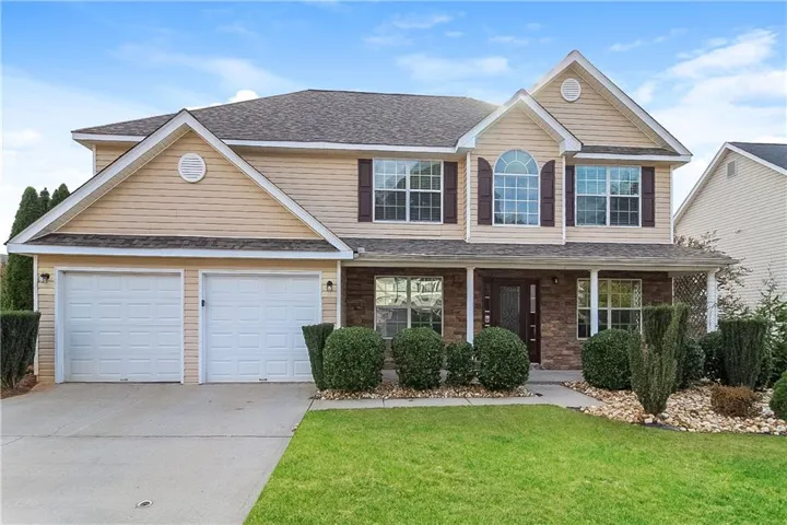 Two-story exterior featuring tan siding, a covered front porch, a two-car garage, and an arched window