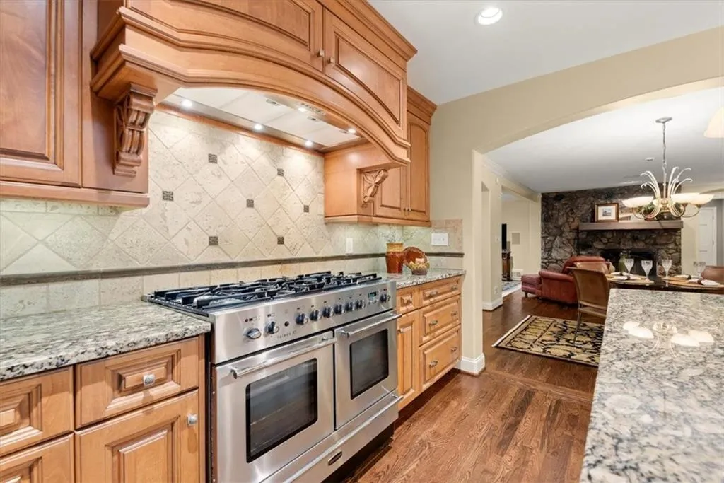 Kitchen with dark hardwood / wood-style flooring, range with two ovens, backsplash, light stone countertops, and premium range hood