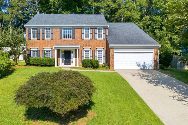 Traditional brick exterior with dark shutters, a covered front entry, and a two-car garage