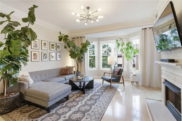 Light wood-finish flooring, bay window with multiple panes, decorative fireplace with mantel, crown molding, and a modern sputnik-style chandelier
